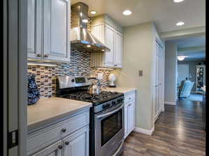 Kitchen featuring white cabinetry, stainless steel gas range oven, dark wood-type flooring, and wall chimney exhaust hood