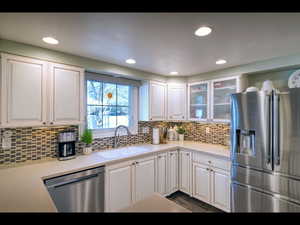 Kitchen with tasteful backsplash, sink, white cabinets, and appliances with stainless steel finishes