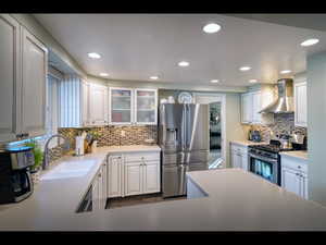 Kitchen with white cabinetry, stainless steel appliances, sink, and wall chimney range hood