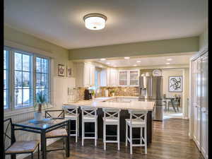 Kitchen with stainless steel fridge with ice dispenser, white cabinetry, backsplash, a kitchen bar, and kitchen peninsula