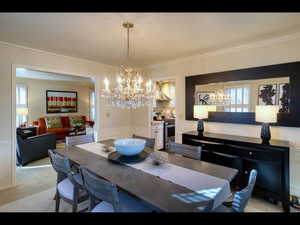 Carpeted dining room with a notable chandelier, a wealth of natural light, and ornamental molding