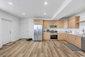 Kitchen with appliances with stainless steel finishes, light brown cabinetry, sink, and light wood-type flooring