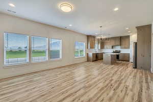 Kitchen with appliances with stainless steel finishes, a chandelier, a kitchen island, light countertops, and light wood-style flooring