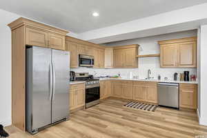 Kitchen featuring light brown cabinetry, sink, light hardwood / wood-style flooring, and stainless steel appliances