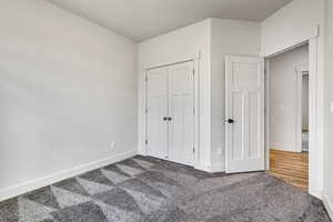 Unfurnished bedroom with dark carpet, baseboards, and a closet