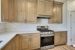 Kitchen featuring stainless steel gas stove, custom range hood, light stone countertops, and light wood-type flooring