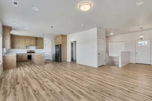 Kitchen with stainless steel stove, black refrigerator with ice dispenser, open floor plan, light countertops, and light wood-style flooring