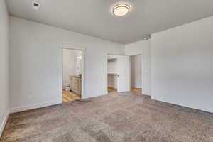 Unfurnished bedroom with light colored carpet, baseboards, connected bathroom, and a spacious closet
