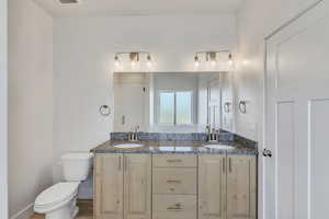 Bathroom featuring toilet, double vanity, a shower, and baseboards