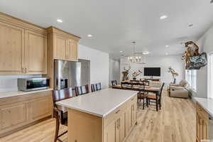 Kitchen featuring a kitchen bar, a center island, hanging light fixtures, light wood-type flooring, and appliances with stainless steel finishes