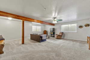 Living area featuring light carpet, ceiling fan, beamed ceiling, and a textured ceiling