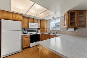 Kitchen with sink, tasteful backsplash, light hardwood / wood-style flooring, a textured ceiling, and white appliances