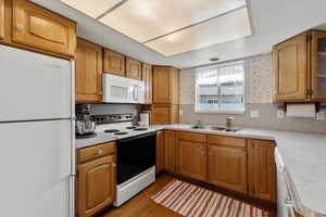 Kitchen featuring white appliances, light hardwood / wood-style floors, sink, and backsplash