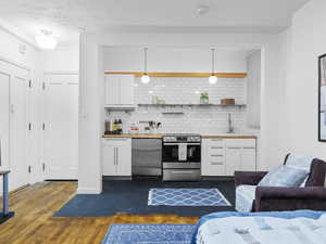 Kitchen with tasteful backsplash, hanging light fixtures, dishwashing machine, stainless steel electric stove, and white cabinets