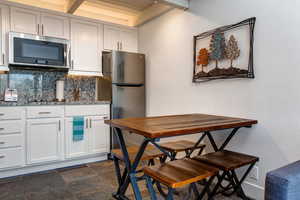 Kitchen featuring white cabinetry, backsplash, granite countertops, and appliances with stainless steel finishes