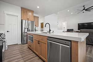 Kitchen with tasteful backsplash, sink, dark hardwood / wood-style flooring, stainless steel appliances, and a center island with sink