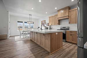 Kitchen with premium range hood, dark wood-type flooring, decorative light fixtures, a center island with sink, and appliances with stainless steel finishes