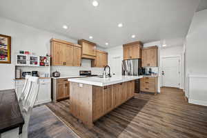 Kitchen with stainless steel appliances, an island with sink, sink, and dark wood-type flooring