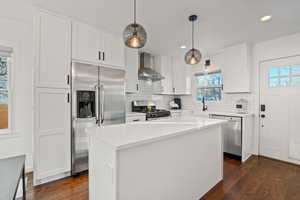 Kitchen featuring appliances with stainless steel finishes, dark hardwood / wood-style floors, pendant lighting, a center island, and wall chimney exhaust hood