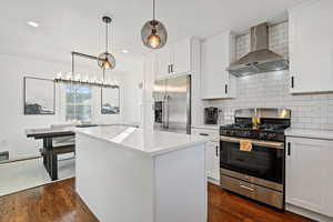 Kitchen with white cabinetry, appliances with stainless steel finishes, decorative backsplash, and wall chimney range hood