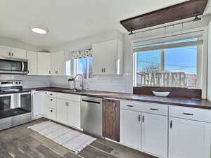 Kitchen featuring appliances with stainless steel finishes, white cabinetry, dark hardwood / wood-style flooring, sink, and backsplash