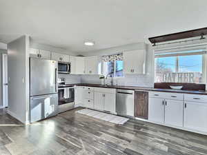 Kitchen with appliances with stainless steel finishes, tasteful backsplash, white cabinets, sink, and dark hardwood / wood-style flooring