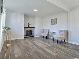 Living area featuring a stone fireplace, beamed ceiling, and wood-type flooring