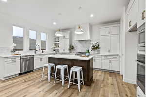 Kitchen featuring modern pendant lighting, light cabinets, a center island, stainless steel appliances, and a walk-in pantry on the right