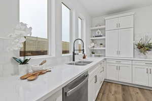 Kitchen with sink, white cabinetry, light stone counters, light hardwood / wood-style flooring, and dishwasher