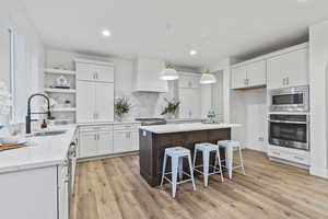 Kitchen with sink facing windows to the Oquirrh Mountains, appliances with stainless steel finishes, white cabinetry, custom range hood, and a kitchen island