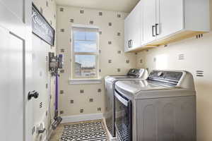 Clothes washing area featuring washing machine and dryer, cabinets, and light tile patterned flooring