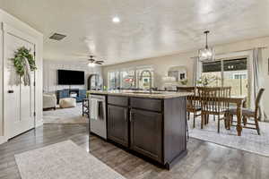 Kitchen with sink, decorative light fixtures, dark brown cabinets, dishwasher, and an island with sink