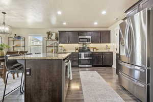 Kitchen featuring appliances with stainless steel finishes, decorative light fixtures, sink, a kitchen bar, and light stone countertops