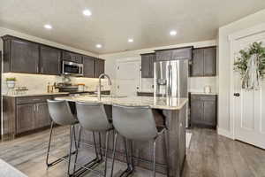 Kitchen featuring sink, light hardwood / wood-style flooring, a breakfast bar, appliances with stainless steel finishes, and an island with sink