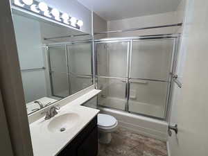 Full bathroom with toilet, vanity, and shower / bath combination with glass door