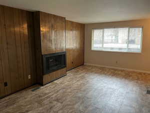 Unfurnished living room featuring wooden walls and a large fireplace