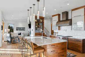 Kitchen featuring sink, a breakfast bar area, a center island with sink, decorative light fixtures, and custom exhaust hood