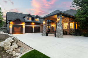 View of front of house featuring concrete driveway, roof with shingles, stone siding, and covered porch