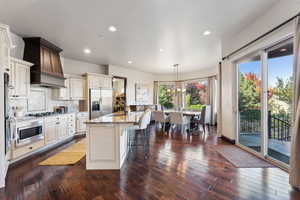 Kitchen featuring a breakfast bar area, built in appliances, hanging light fixtures, a center island with sink, and light stone countertops