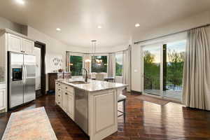 Kitchen featuring stainless steel appliances, a sink, light stone countertops, an island with sink, and dark wood-style flooring