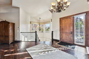 Foyer featuring an inviting chandelier, vaulted ceiling, dark wood-type flooring, and a wealth of natural light