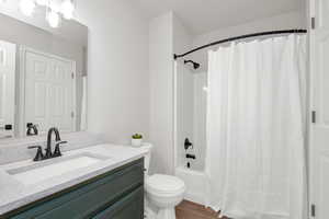 Full bathroom with hardwood / wood-style flooring, vanity, shower / bathtub combination with curtain, and toilet