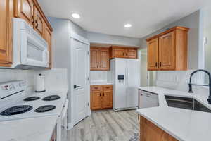 Kitchen with white appliances, light hardwood / wood-style floors, sink, and backsplash