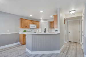 Kitchen with light wood-type flooring, sink, white appliances, and kitchen peninsula