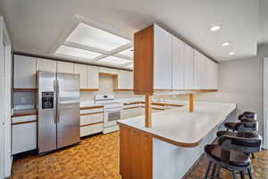 Kitchen featuring light parquet floors, white range with electric stovetop, stainless steel refrigerator with ice dispenser, white cabinets, and kitchen peninsula