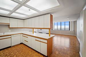 Kitchen featuring white dishwasher, coffered ceiling, white cabinets, kitchen peninsula, and light parquet flooring