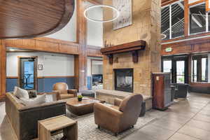 Tiled living room with a towering ceiling, a stone fireplace, and wooden walls