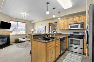 Kitchen with light brown cabinetry, sink, decorative light fixtures, kitchen peninsula, and stainless steel appliances