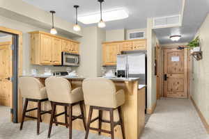 Kitchen with light brown cabinetry, decorative light fixtures, a kitchen bar, light stone counters, and stainless steel appliances