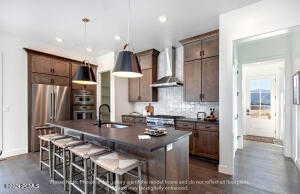 Kitchen featuring sink, decorative light fixtures, a center island with sink, stainless steel refrigerator, and wall chimney range hood